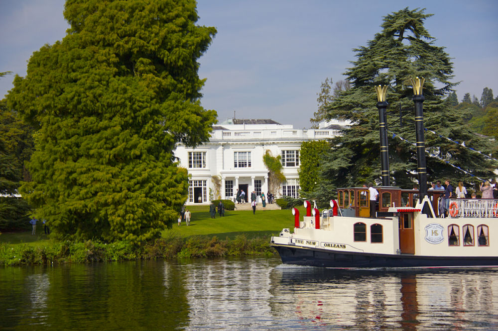 A view of Henley Greenlands campus from the river with a boat passing by